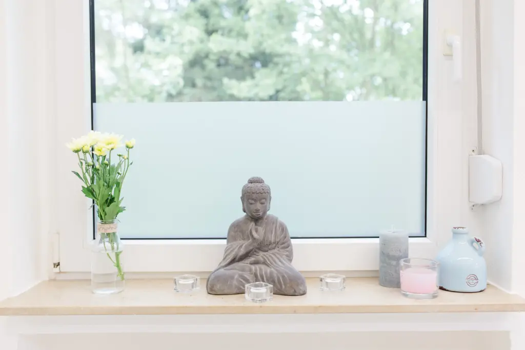 Buddha-Figur und Blumen auf der Fensterbank im Tageslicht des bodymind Kursstudios