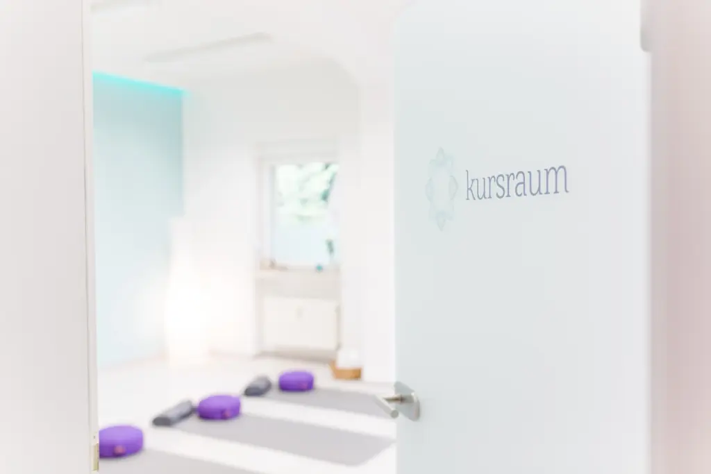 Glastür mit der Aufschrift kursraum, dahinter ausgelegte Yogamatten mit Meditationskissen