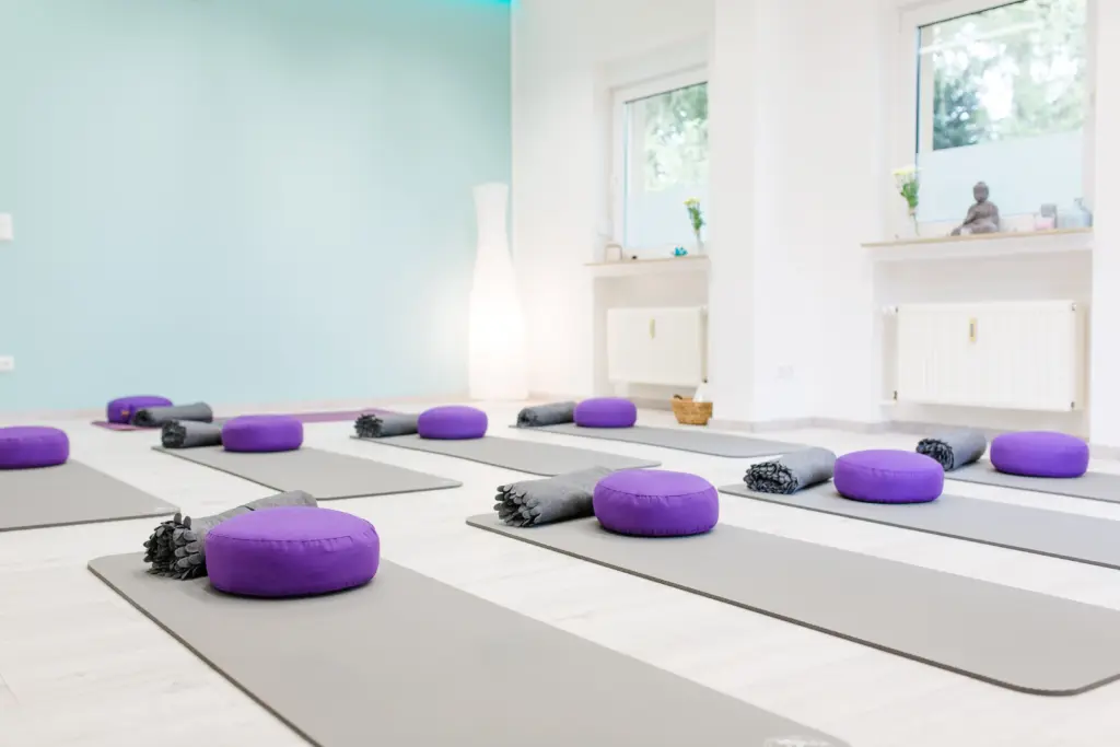 Kursraum des bodymind Kursstudios in Mülheim an der Ruhr mit ausgelegten Yogamatten, lila Meditationskissen und Decken